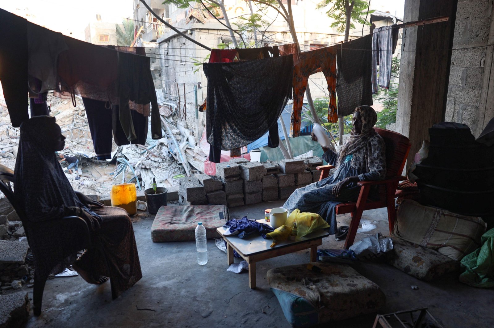 Displaced Palestinian women sit near hanging laundry inside a damaged building in which they took refuge, al-Bureij refugee camp, Gaza, Palestine, June 12, 2024. (AFP Photo)