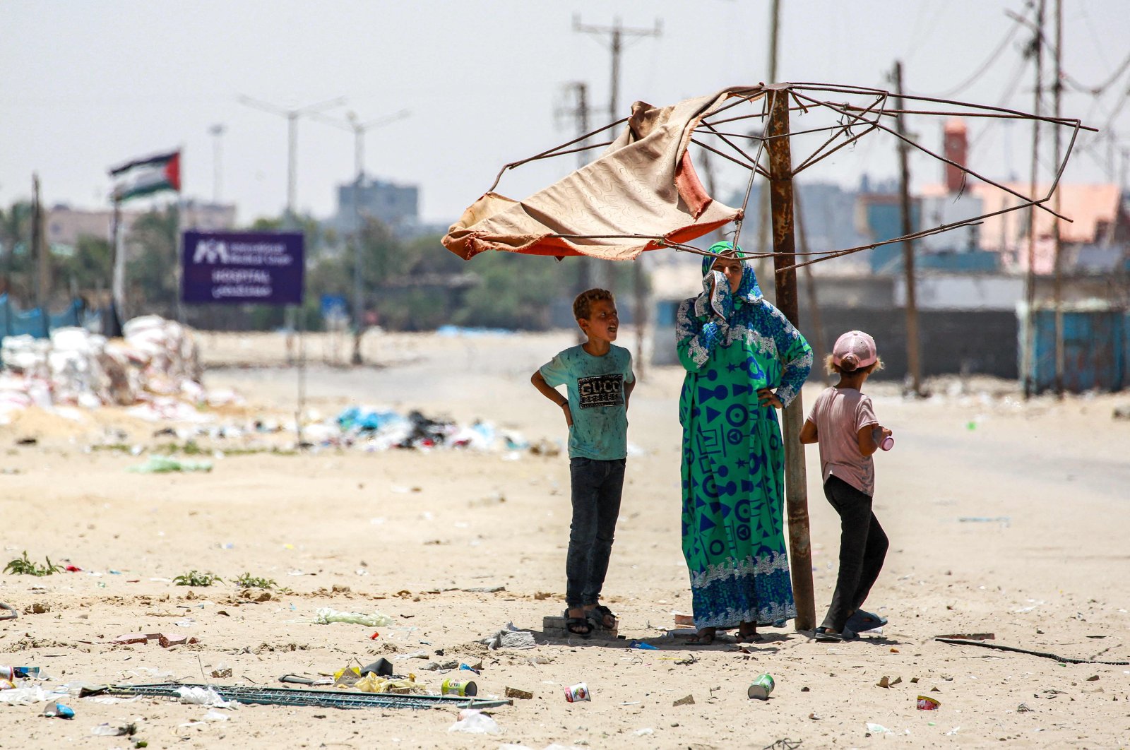 A woman stands with two children under a fraying shade along a street in the western part of Rafah in the southern Gaza Strip, Palestine, June 14, 2024. (AFP Photo)