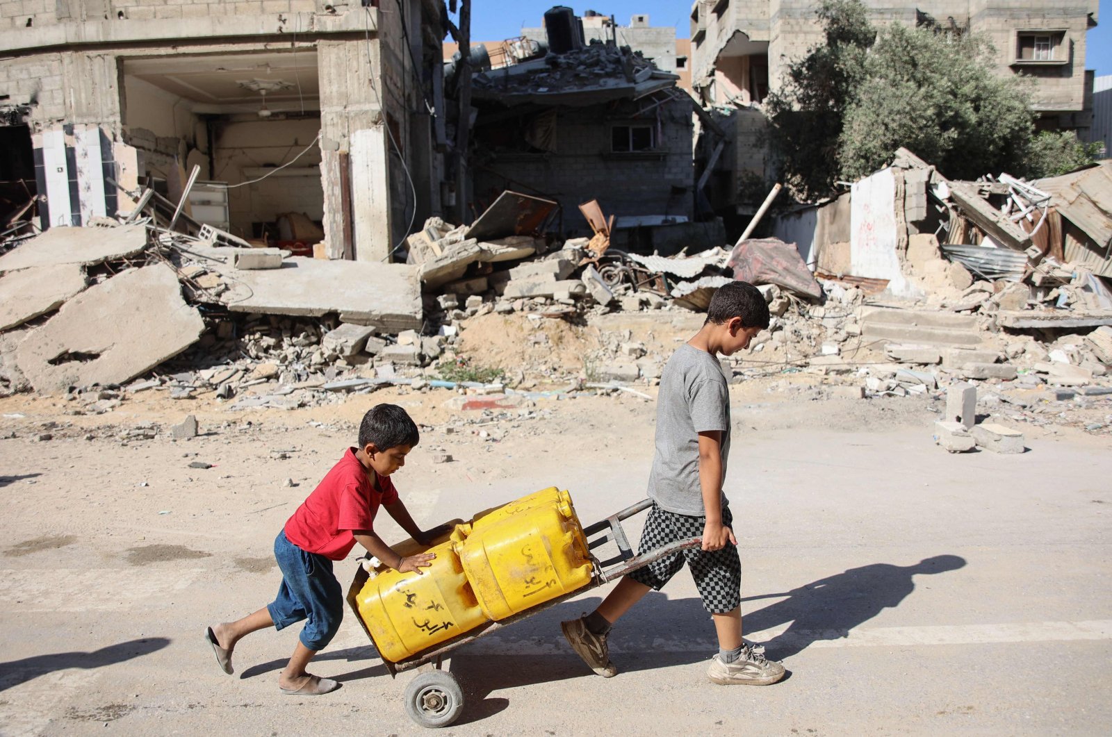 Palestinian boys transport water containers past buildings destroyed during previous Israeli bombardment, in Gaza City, June 10, 2024. (AFP Photo)