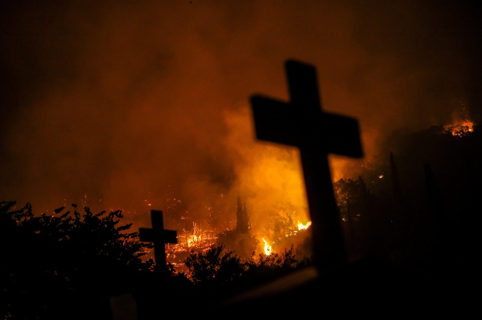 Crosses from graves are silhouetted as a wildfire burns in the village of Latas, Greece, June 22, 2024. (Reuters Photo)