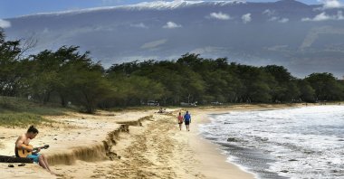 Snow-capped Haleakala serves as a backdrop as Paia, Maui's Scott Picton, (L) plays a guitar and Saskatchewan's Shannon and Dan Runcie walk on Sugar Beach in South Maui, Hawaii, Feb. 11, 2019. (AP Photo)