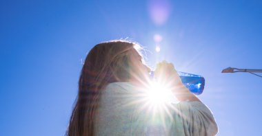 A woman drinking water outside while being illuminated by a ray of sunlight, Dec. 31, 2020. (Getty Images)