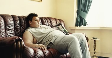 A young man indulges in inactivity, slouching on a sofa while watching videos and holding a packet of chips, Sept. 14, 2005. (Getty Images)