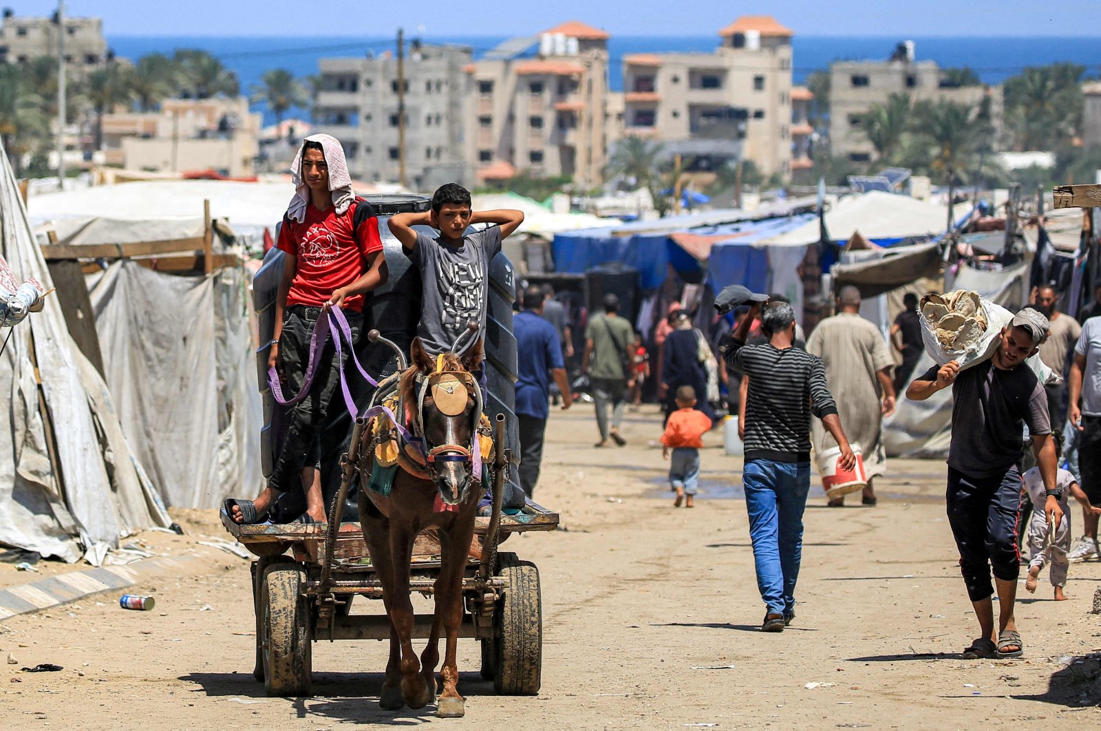 Two boys ride a horse-drawn cart pulling a water cistern past tents sheltering displaced Palestinians, Rafah, Gaza Strip, Palestine, June 25, 2024. (AFP Photo)