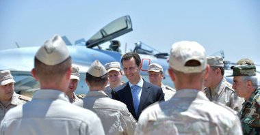  A handout picture released on the official Facebook page of the Syrian Presidency on June 27, 2017, shows President Bashar Assad (C) being welcomed by a Russian soldier during his visit to the Hmeimim military base in Latakia province, in the northwest of Syria. The Paris appealS court validated on June 26, 2024an arrest warrant for Syrian President Bashar Assad that France issued last year for alleged complicity in war crimes during Syria's civil war, according to plaintiffs lawyers. (Photo by Syrian Presidency Facebook page / AFP)