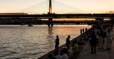People sit and fish on the banks of the Golden Horn estuary at sunset, as the Golden Horn Metro Bridge is seen in the background in the Karaköy district in Istanbul, Türkiye, June 17, 2024. (AFP Photo)