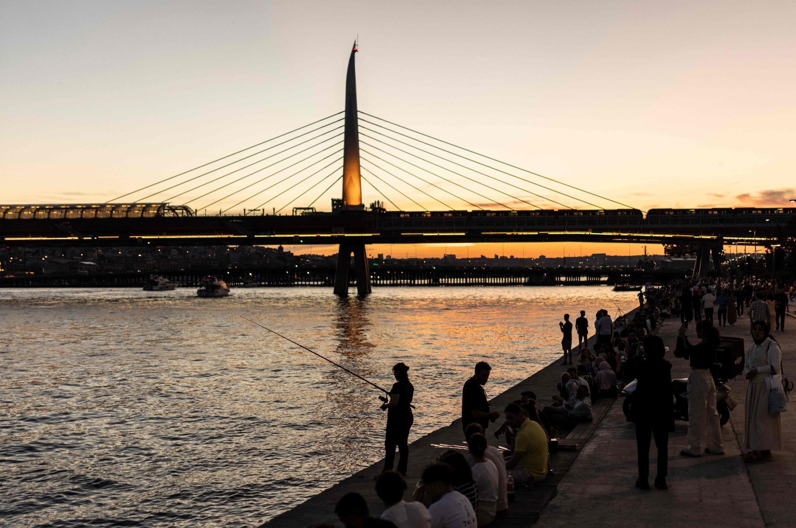 People sit and fish on the banks of the Golden Horn estuary at sunset, as the Golden Horn Metro Bridge is seen in the background in the Karaköy district in Istanbul, Türkiye, June 17, 2024. (AFP Photo)