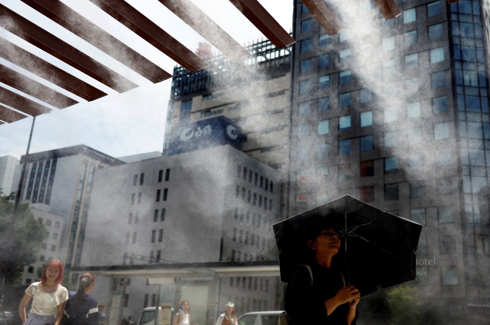 Passersby take a break under a cooling mist as the Japanese government issued a heatstroke alert in Tokyo and other prefectures, Tokyo, Japan, July 9, 2024. (Reuters Photo)