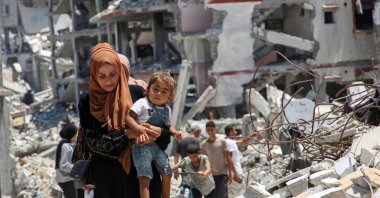 A Palestinian woman holds her daughter as she walks past the rubble of houses destroyed during the Israeli military offensive, Khan Younis, Gaza Strip, Palestine, July 10, 2024. (Reuters Photo)