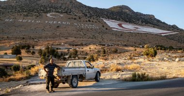 A shepherd poses next to his truck along a road near the village of Kaynakköy, known in Greek as Sychari, close to the giant flag of the Turkish Republic of Northern Cyprus (TRNC) painted on the side of the Kyrenia mountain range in the northern part of the divided Mediterranean island of Cyprus, July 8, 2024. (AFP Photo)