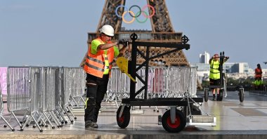 A worker stands on the Trocadero with the Eiffel Tower, bearing the Olympics rings, seen in the background ahead of the Paris 2024 Olympic and Paralympic games, in Paris on July 19, 2024. (Photo by MANAN VATSYAYANA / AFP)