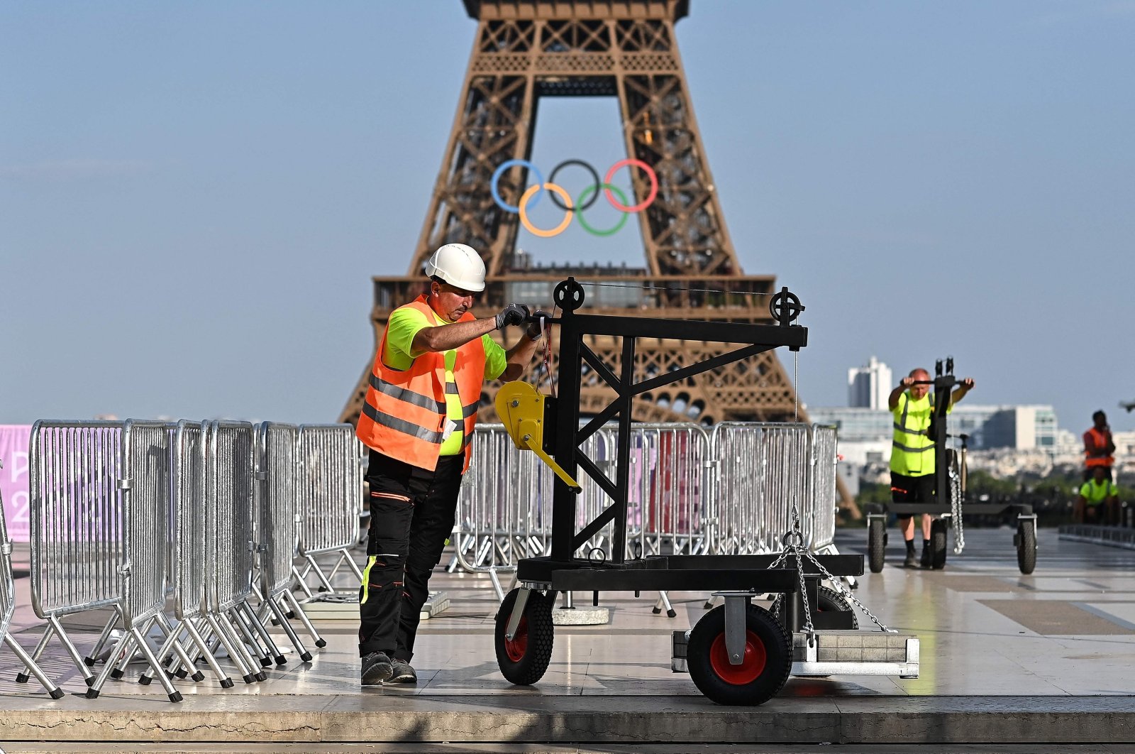 A worker stands on the Trocadero with the Eiffel Tower, bearing the Olympics rings, seen in the background ahead of the Paris 2024 Olympic and Paralympic games, in Paris on July 19, 2024. (Photo by MANAN VATSYAYANA / AFP)