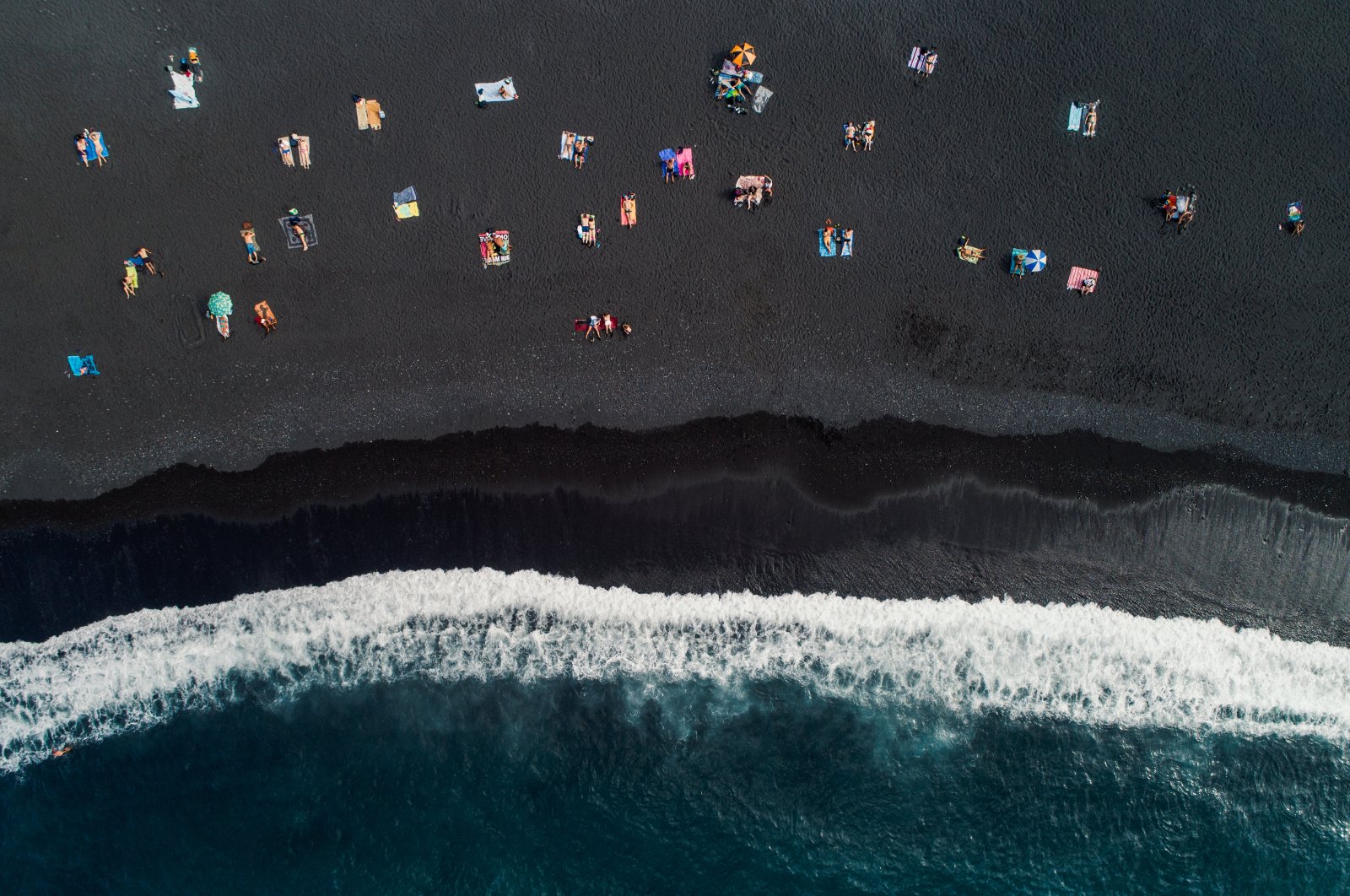 Sunbathers on a black sand beach photographed from directly above, Tenerife, Spain, Oct. 11, 2021. (Getty Images)