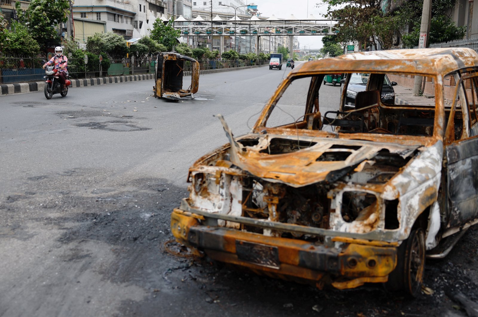 A man rides his motorbike past burned vehicles that was set afire by a mob during student protests against government job quotas, in Dhaka, Bangladesh, July 22, 2024. (Reuters Photo)