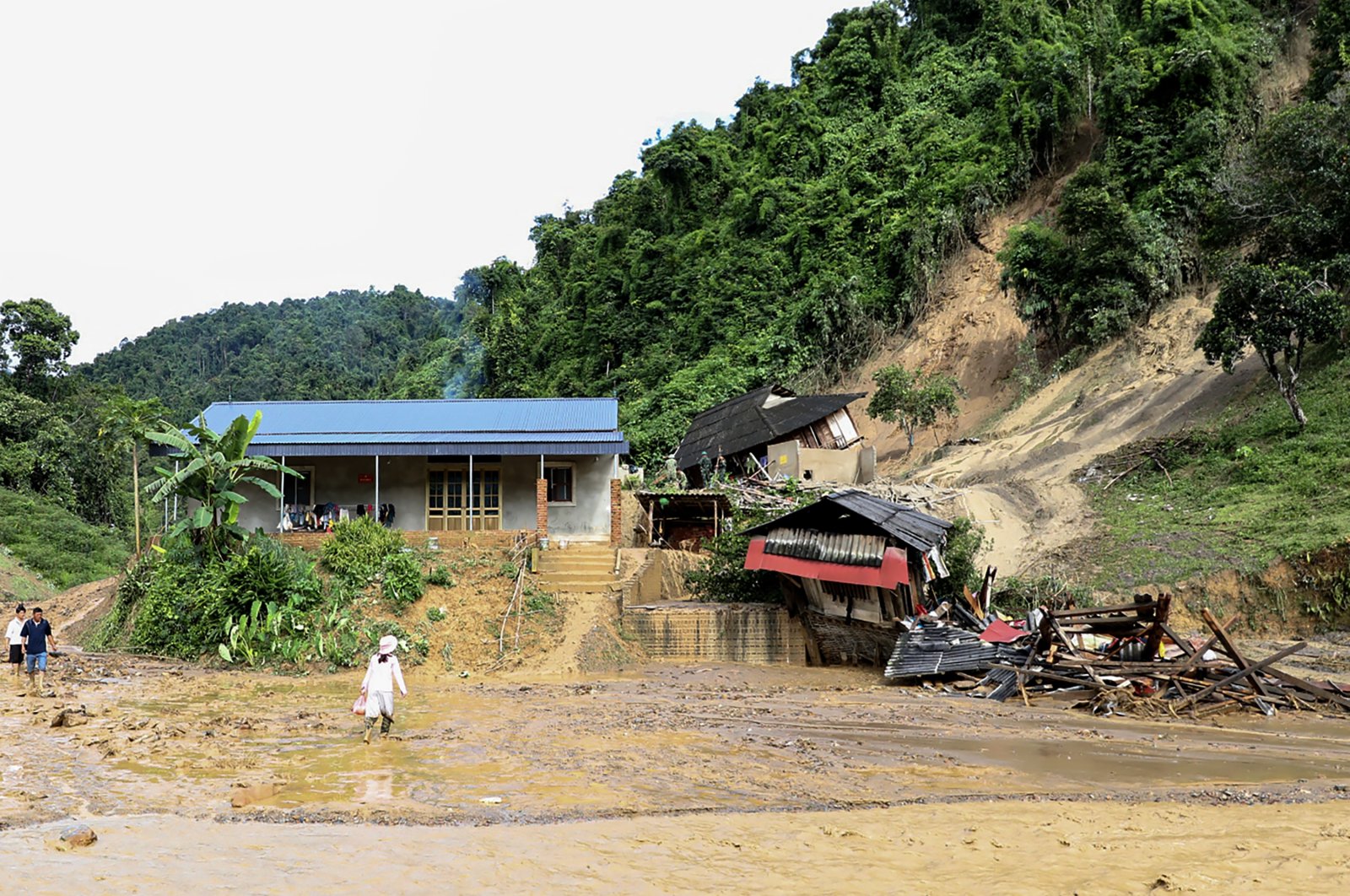 People walk through the mud past debris of property damaged by a landslide, Dien Bien province, Vietnam, July 25, 2024. (AFP Photo)