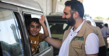 A Humanitarian Relief Foundation (IHH) official reacts to an Iraqi child waving as a group of displaced Iraqis crosses the Tal Abyad border gate to return home to Iraq, northern Syria, July 29, 2024. (AA Photo)