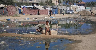 A Palestinian boy smiles to the camera as he sits on a street flooded with sewage water in Deir el-Balah in the central Gaza Strip, Palestine, July 23, 2024. (AFP Photo)