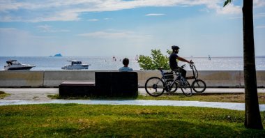 A cyclist takes a break and sits on the bench while another cyclist is passing him by at the Caddebostan beach, Kadıköy, Istanbul, Türkiye, Aug. 11, 2023 (Getty Images Photo)
