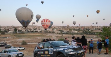 A rally car waits with hot air balloons in the background, Cappadocia, Türkiye, Aug. 6, 2024. (IHA Photo)