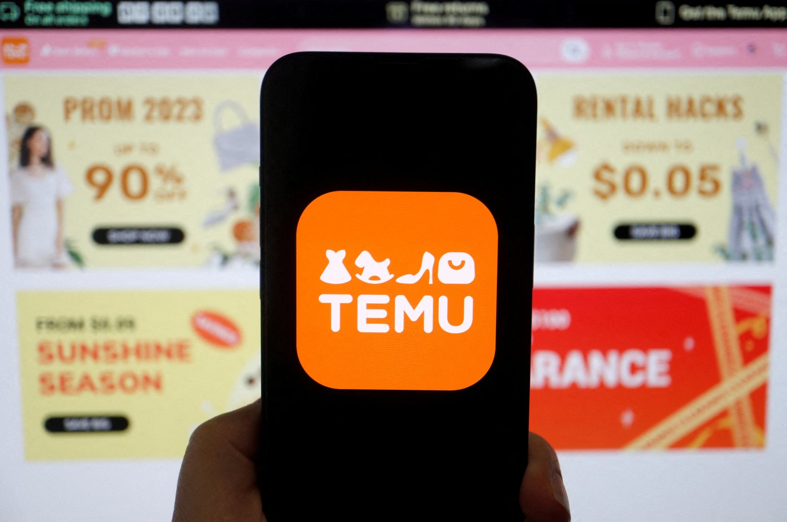 The logo of Temu, an e-commerce platform owned by PDD Holdings, is seen on a mobile phone displayed in front of its website, in this illustration picture taken April 26, 2023. (Reuters Photo)