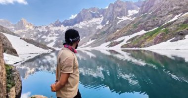 One of the mountaineers looks out over the glacial lake, Hakkari, Türkiye, Aug. 7, 2024. (IHA Photo)