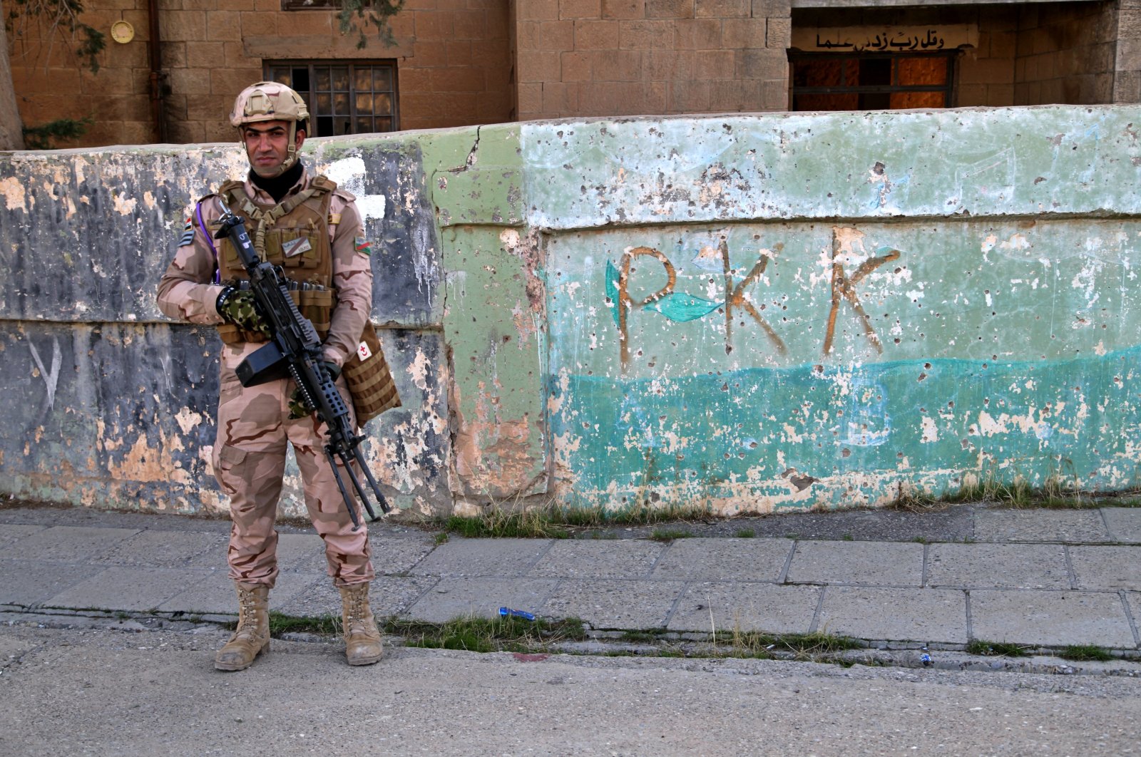 An Iraqi army soldier stands next to the graffiti left by an affiliate of the PKK terrorist group, which withdrew in Sinjar, Iraq, Dec. 4, 2020. (AP Photo)