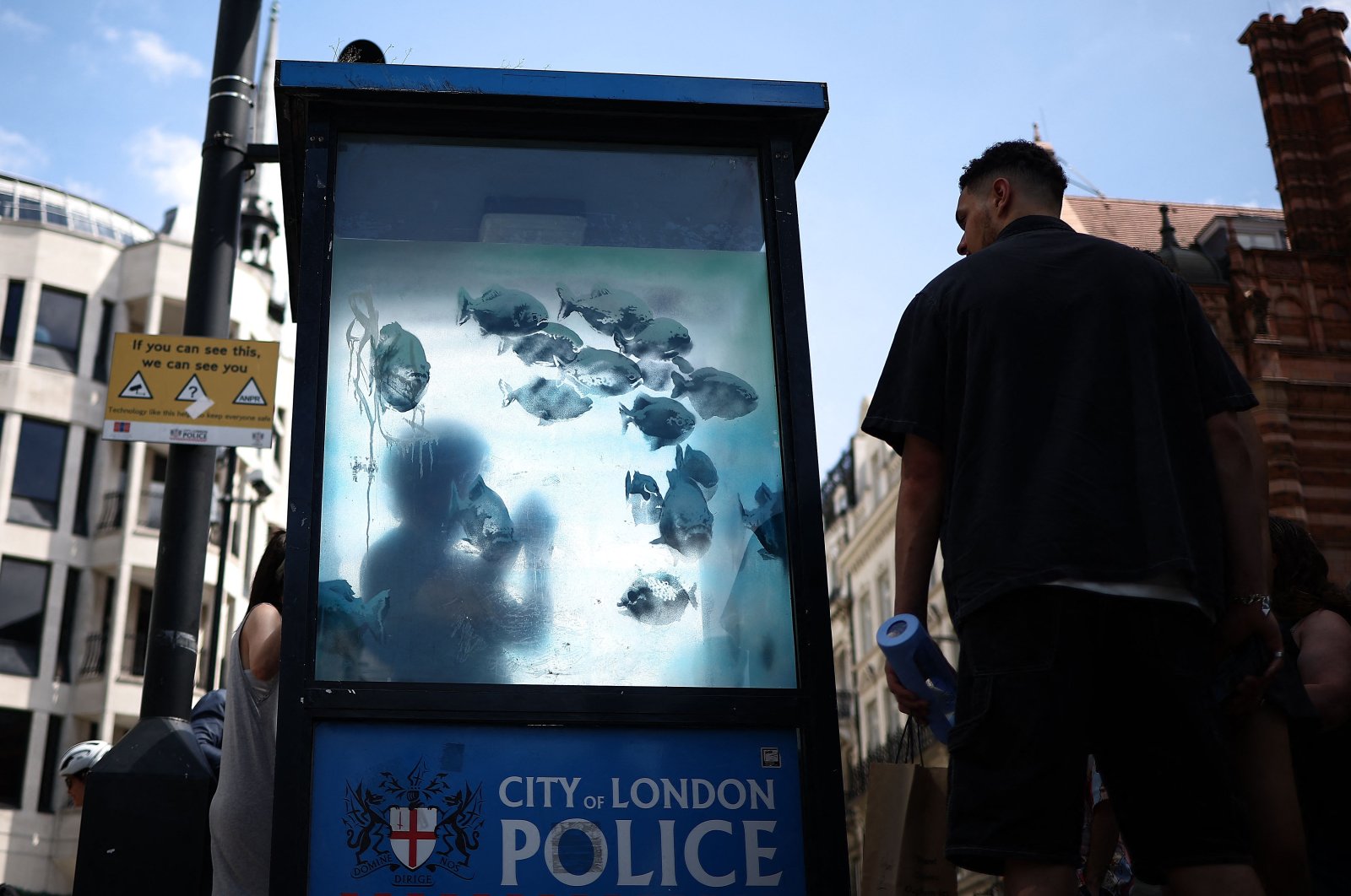 A pedestrian stops to look at an artwork by street artist Banksy, the seventh released this week, depicting fish swimming around a Police Box, City of London, U.K., Aug. 11, 2024. (AFP Photo)