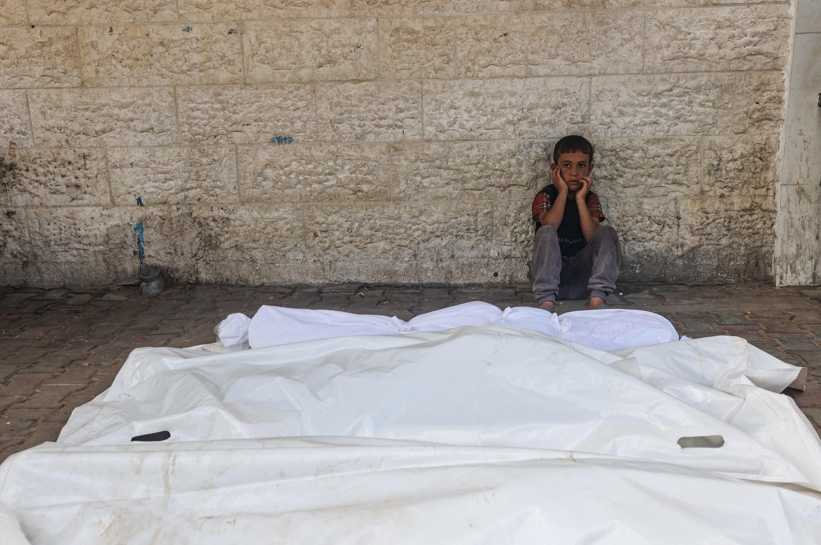 This file photo shows a child sitting beside the shrouded corpses of people killed in an overnight Israeli strike, in Deir el-Balah, central Gaza Strip, Aug. 10, 2024. (AFP Photo)