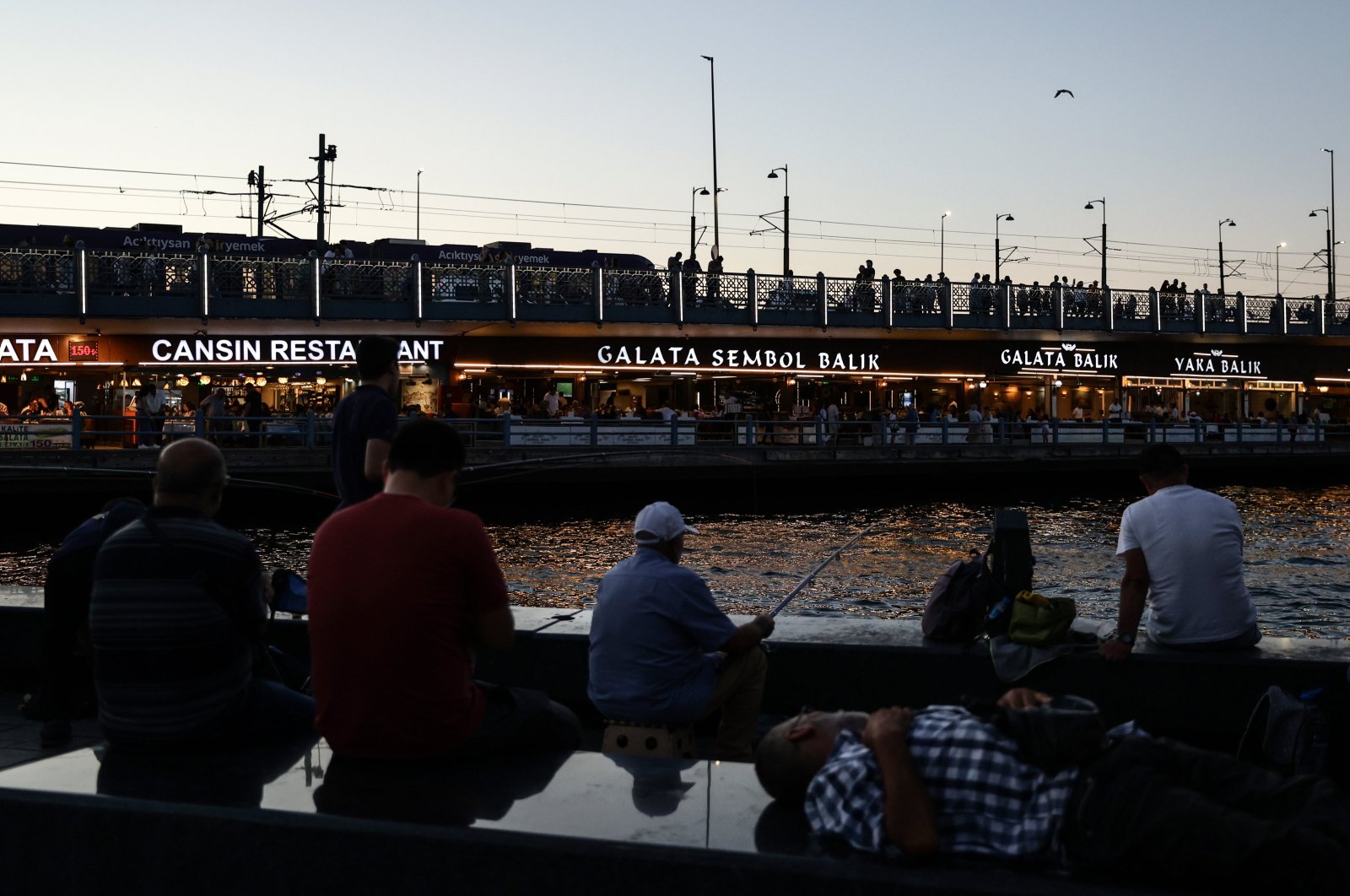 People rest near the Bosporus, backdropped by the Galata Bridge, during sunset, Istanbul, Türkiye, Aug. 15, 2024. (EPA Photo)