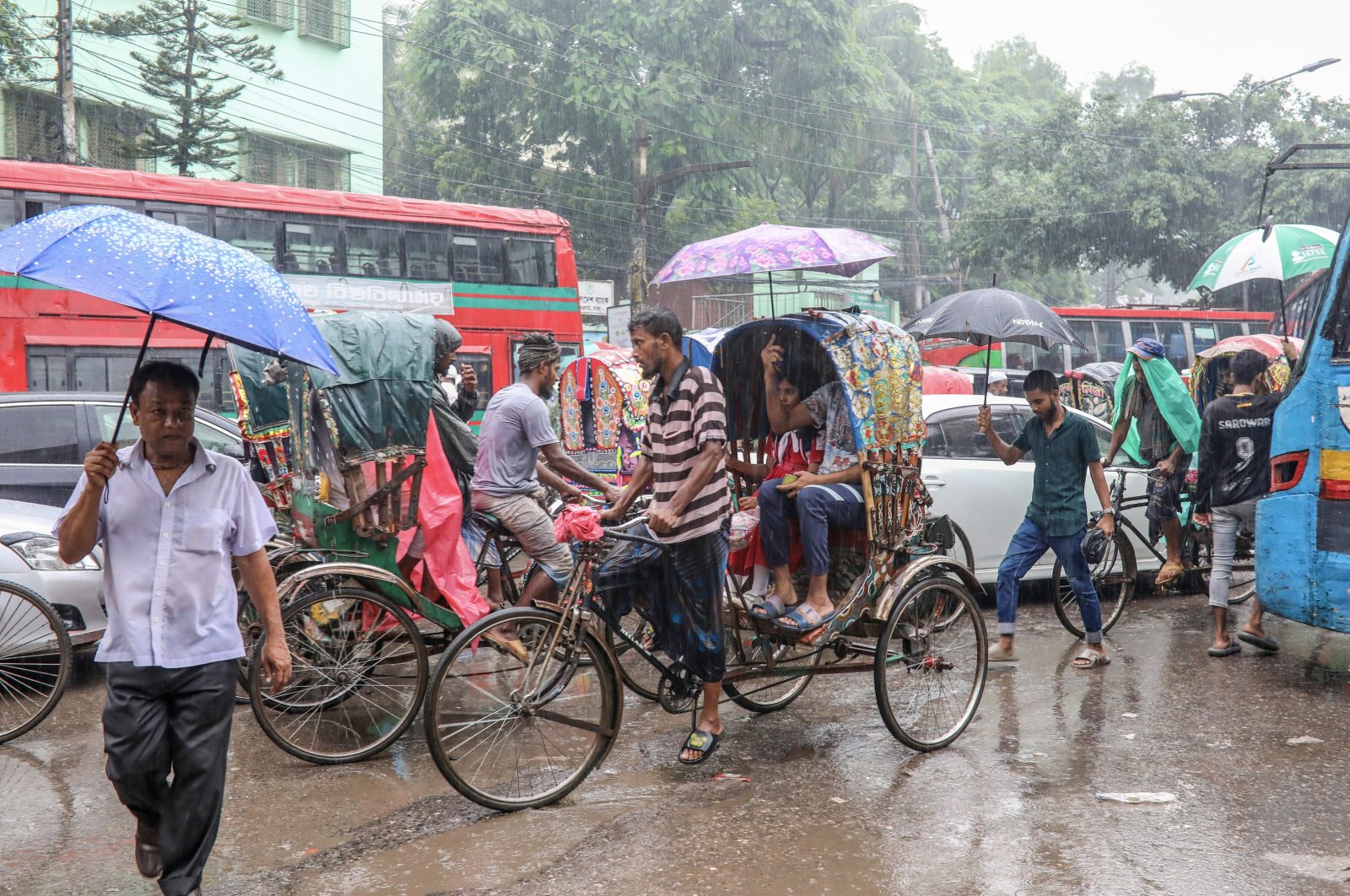 People shelter under umbrellas during rainfall as they walk and ride along a street, Dhaka, Bangladesh, Aug. 21, 2024. (EPA Photo)