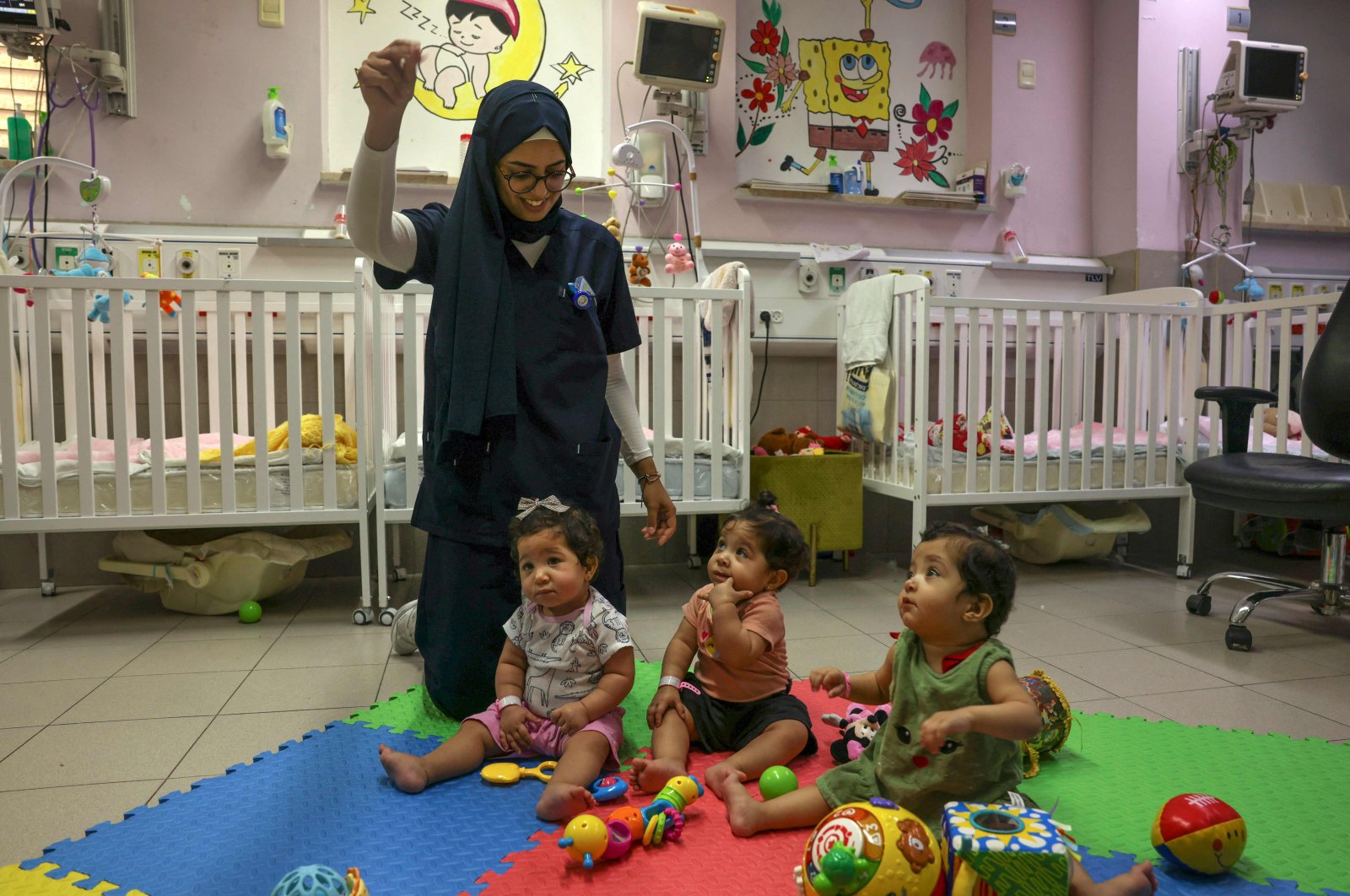 A nurse entertains Palestinian triplets of Gaza-native Hanane Bayouk, Najmeh (L), Najoua (C) and Noor, at the children&#039;s ward of the Al-Maqased Hospital, Jerusalem, Palestine, July 31, 2024. (AFP Photo)