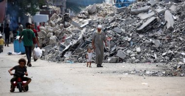 An elderly man holds a child by the hand as he walks past a building levelled by Israeli bombardment in the Bureij refugee camp in central Gaza Strip, Palestine, Aug. 25, 2024. (AFP Photo)