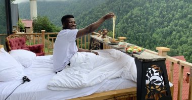 Ghanaian tourist Yahya Abulli enjoys breakfast on the balcony of a wooden bungalow, Rize, northern Türkiye, Aug. 27, 2024. (DHA Photo)