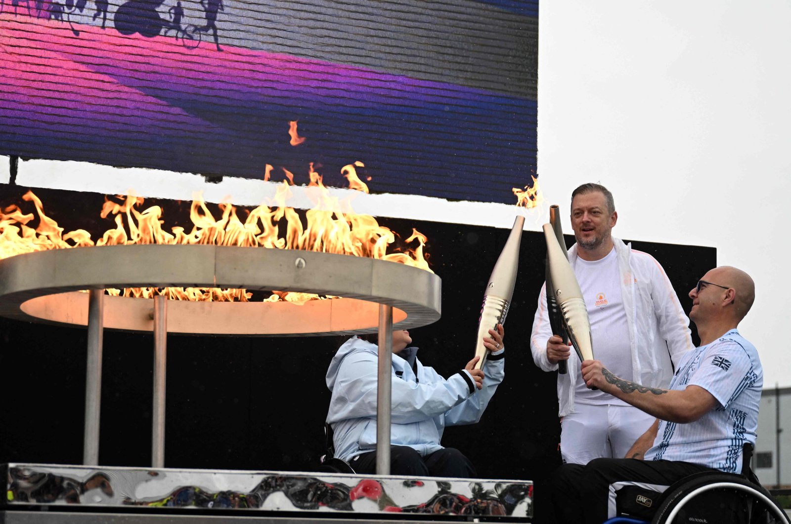 Britain&#039;s Helene Raynsford (L) and Britain&#039;s Gregor Ewan, light the torch of International Paralympic Committee President Andrew Parsons (C), lit from the cauldron, during the Paralympic torch-lighting ceremony at Stoke Mandeville, Aylesbury, U.K., Aug. 24, 2024. (AFP Photo)