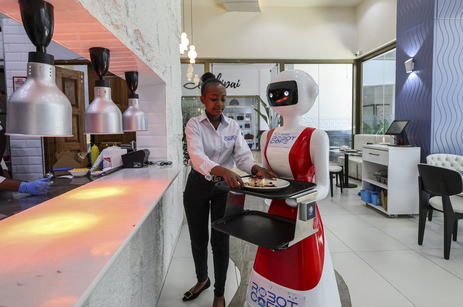 A human waiter is loading a robotic waiter (C) with a food order to deliver to a customer at the Robot Cafe, Kileleshwa, Nairobi, Kenya, Aug. 29, 2024. (EPA Photo)