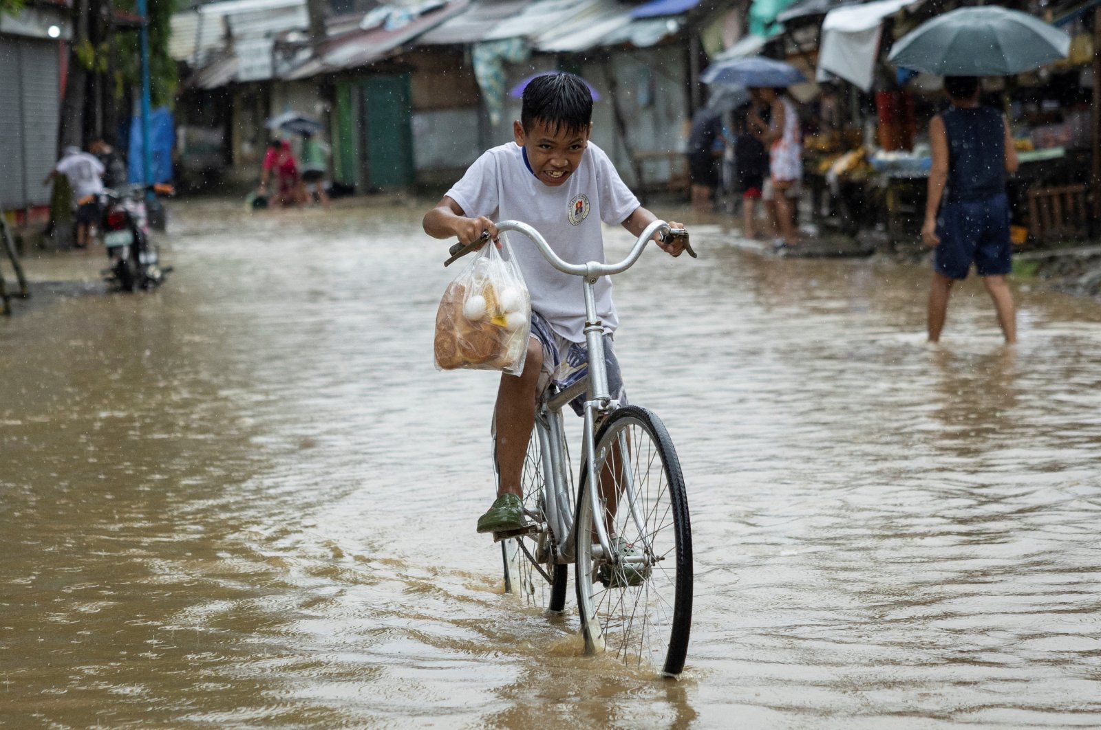 A boy rides his bike through a flooded road with bread and eggs after heavy rains from Tropical Storm Yagi, Rizal, Philippines, Sept. 2, 2024. (Reuters Photo)