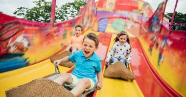Children having fun sliding down a yellow and red slide while sitting in burlap sacks. (Getty Images Photo)