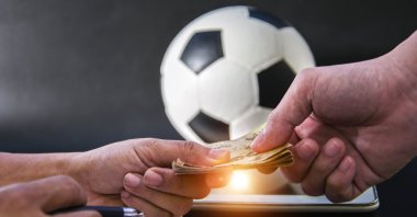 The photo shows two people exchanging money in front of a football and a tablet. (Getty Images Photo)