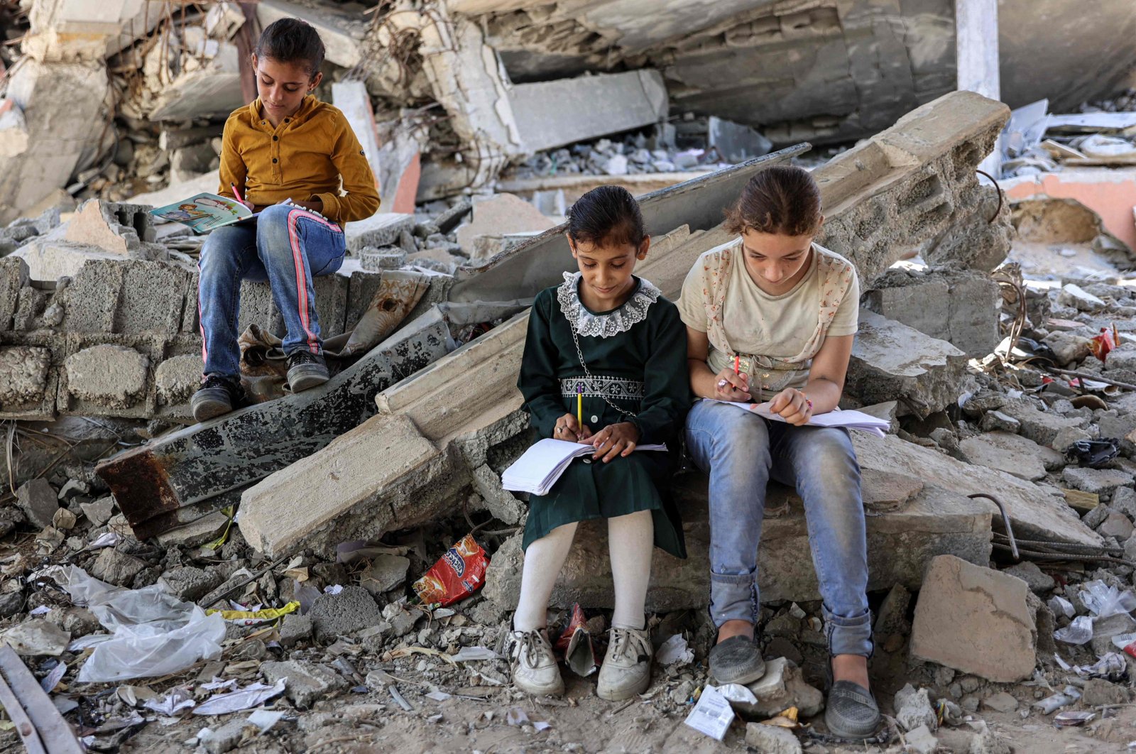 Children write in notebooks by the rubble of buildings destroyed by Israel near a tent being used as a make-shift educational center for primary education students in Jabalia in the northern Gaza Strip, Sept. 8, 2024. (AFP Photo)