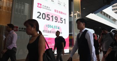 Pedestrians walk past a sign showing the numbers of the Hang Seng Index in Hong Kong, Sept. 27, 2024. (AFP Photo)