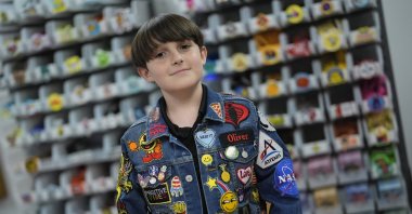Oliver Burkhardt, 13, stands in front of trays of patches inside the offices of the Oliver Patch Project, Florida, U.S., Sept. 4, 2024. (AP Photo)