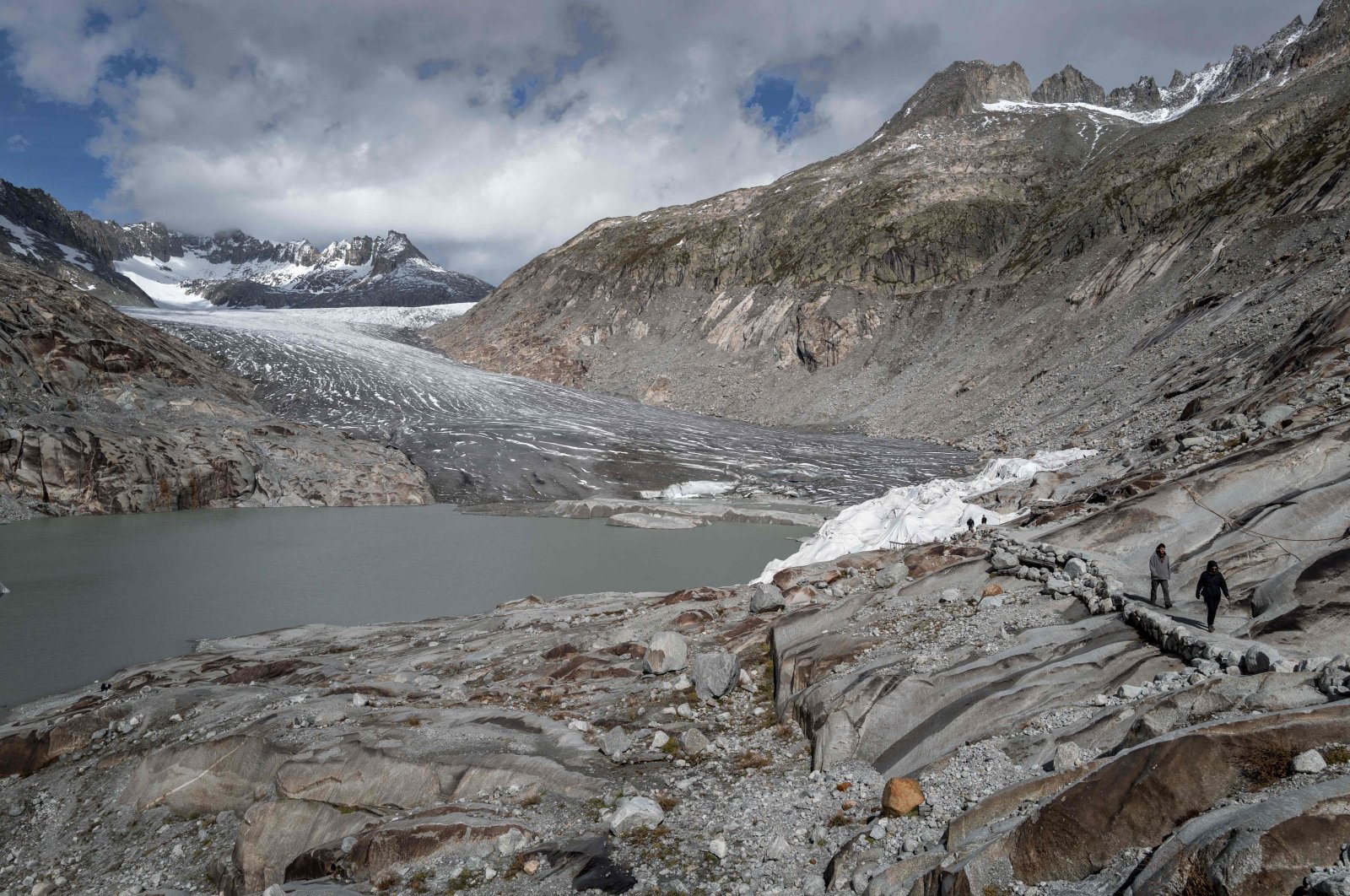 People walk next to the Rhone Glacier and its glacial lake (L), formed by the melting of the glacier due to global warming, near Gletsch, in the Swiss Alps, Switzerland, Sept. 30, 2024. (AFP Photo)