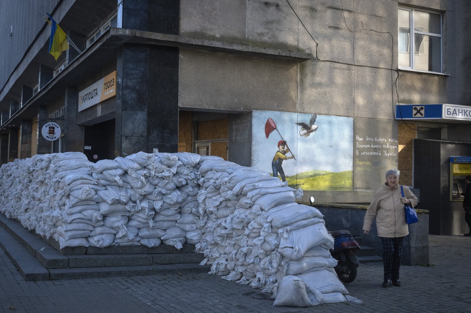 This file photo shows a local resident passing by sandbags protecting the city post office from the Russian army, in Kherson, Ukraine, Nov. 10, 2023. (AP Photo)