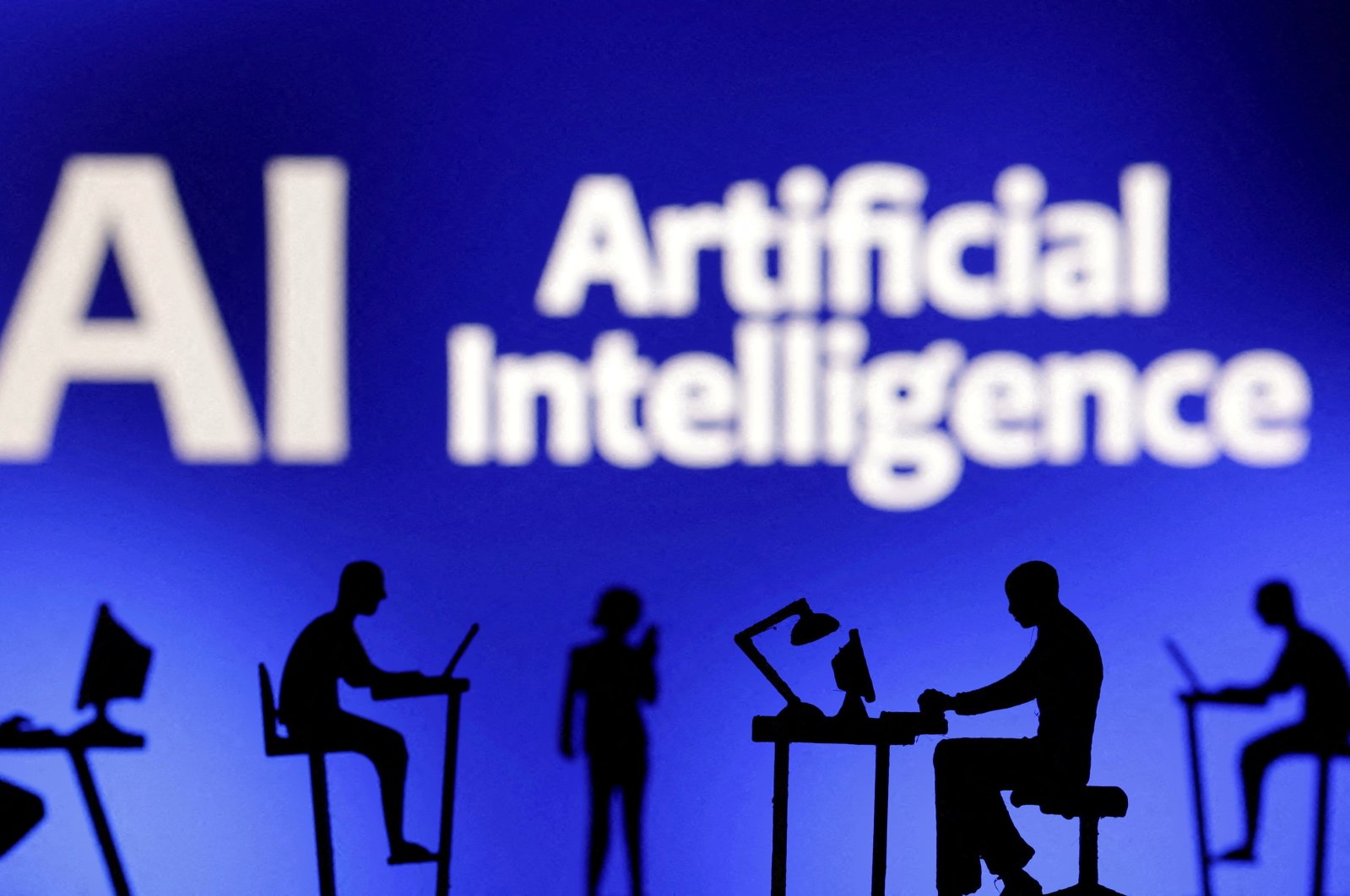 This illustration shows figurines with computers and smartphones in front of the words &quot;AI Artificial Intelligence,&quot; Feb. 19, 2024. (Reuters Photo)