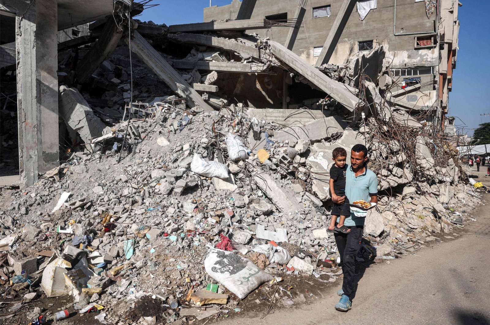 A man carries a child while walking past a collapsed building in the Bureij camp for Palestinian refugees, central Gaza Strip, Palestine, Oct. 9, 2024. (AFP Photo)