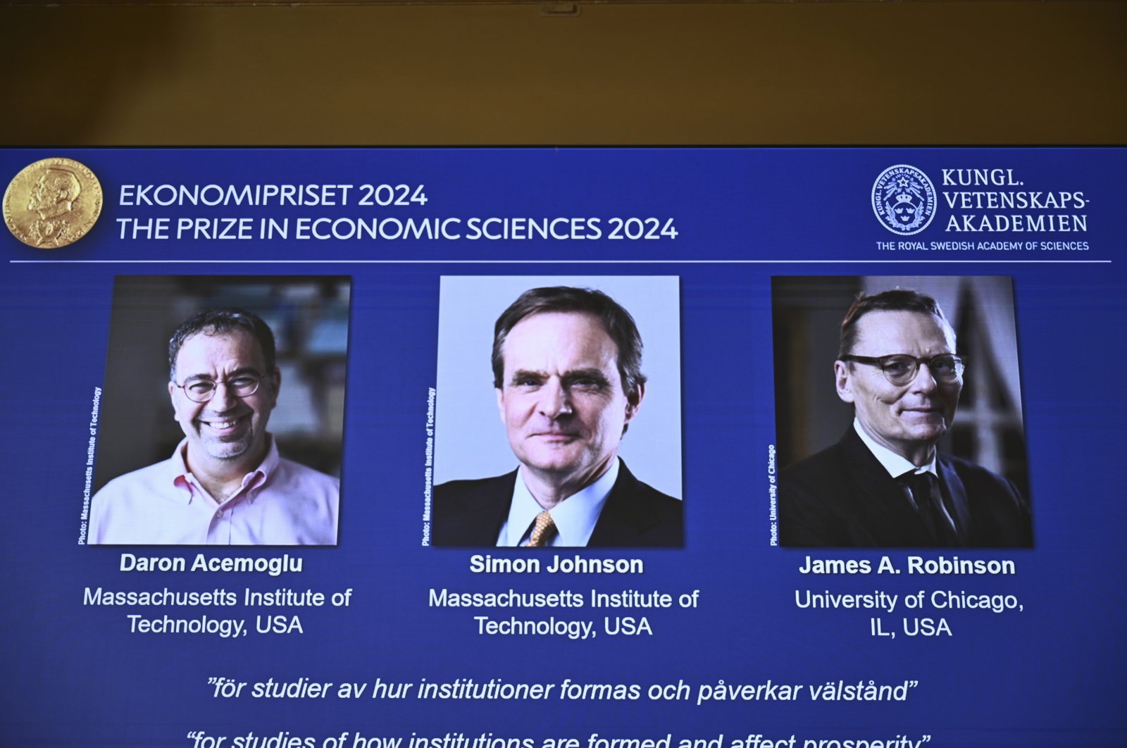 The Nobel Economics Prize is awarded to Daron Acemoğlu, Simon Johnson, and James A Robinson, seen on screen during a press meeting at the Royal Swedish Academy of Sciences in Stockholm, Sweden, Oct. 14, 2024. (TT News Agency via AP)