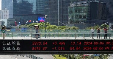 People take pictures on an overpass with a display of stock information in front of buildings in the Lujiazui financial district, Shanghai, China, Aug. 6, 2024. (Reuters Photo)