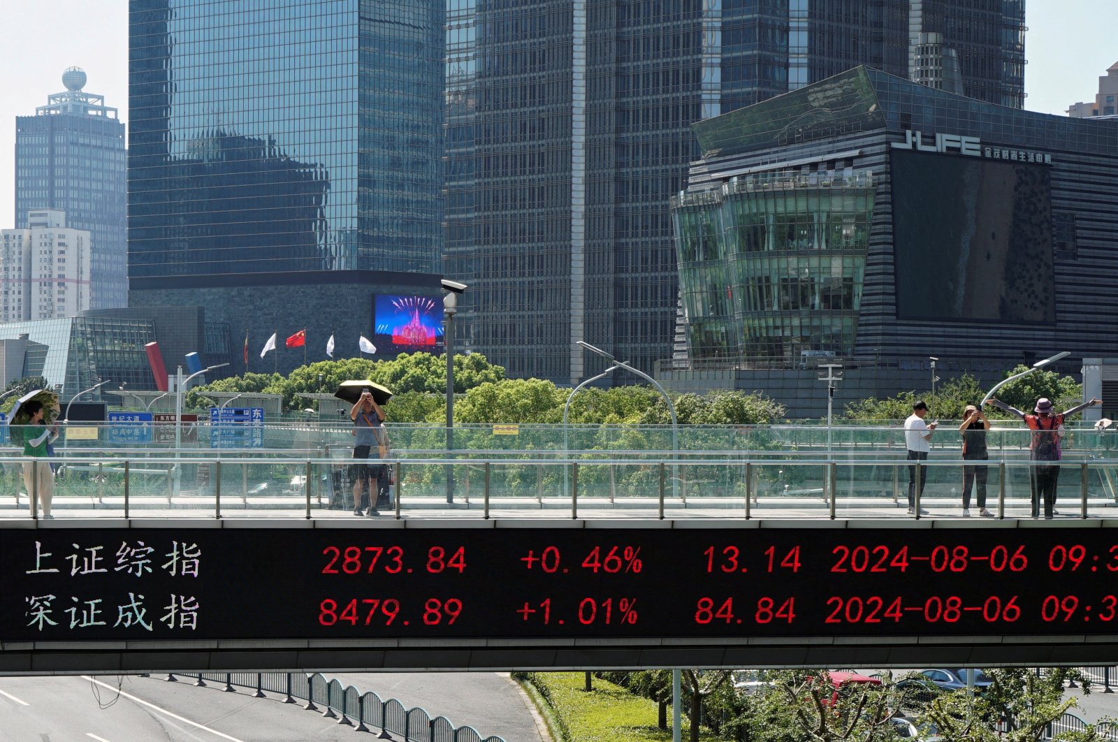 People take pictures on an overpass with a display of stock information in front of buildings in the Lujiazui financial district, Shanghai, China, Aug. 6, 2024. (Reuters Photo)