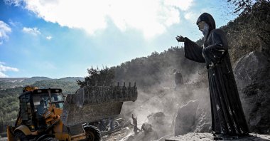 A Statue of the 19th-century Maronite Christian St. Mar Charbel is pictured as a bulldozer moves to clear rubble and debris from the site of a previous Israeli air strike on the village of Aito, northern Lebanon, Oct. 15, 2024. (AFP Photo)