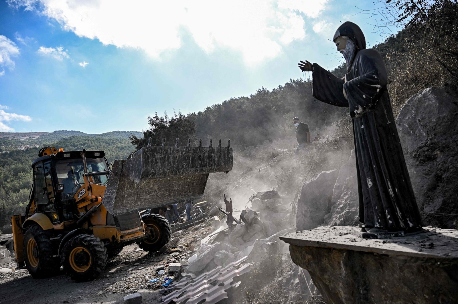 A Statue of the 19th-century Maronite Christian St. Mar Charbel is pictured as a bulldozer moves to clear rubble and debris from the site of a previous Israeli air strike on the village of Aito, northern Lebanon, Oct. 15, 2024. (AFP Photo)